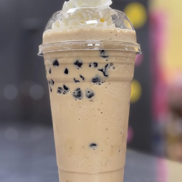 A creamy brown boba drink with whipped cream on top, in a clear plastic cup.