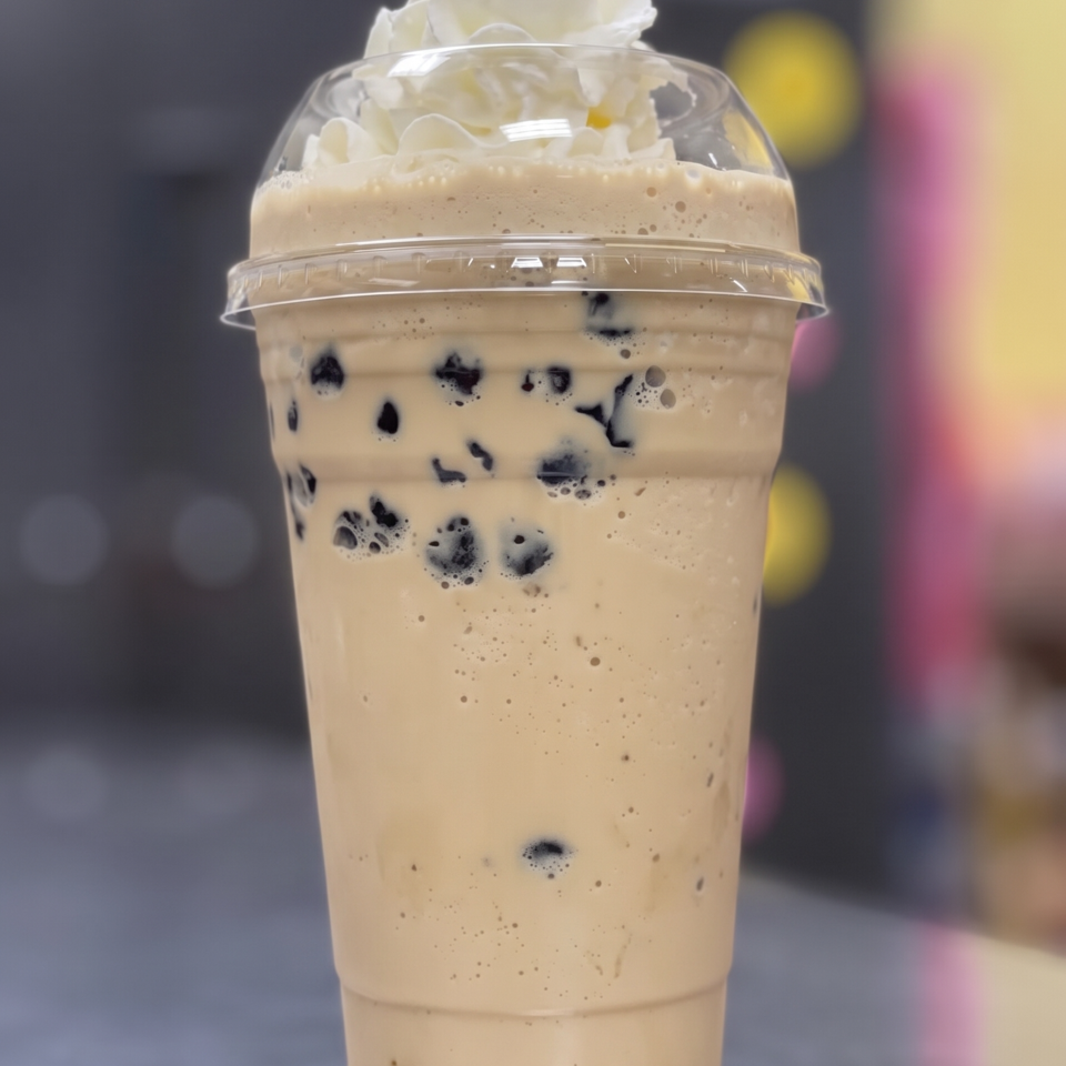 A creamy brown boba drink with whipped cream on top, in a clear plastic cup.