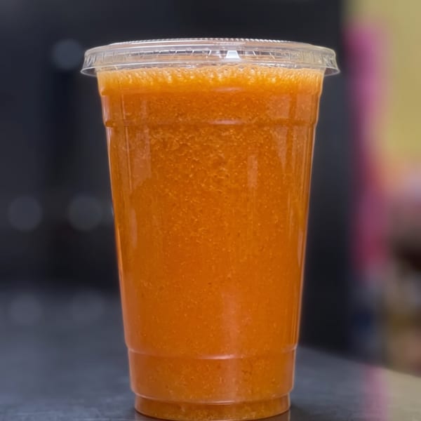 Orange smoothie in a clear plastic cup with a lid, on a dark counter.