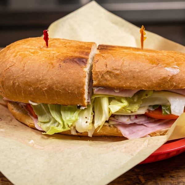 Large submarine sandwich cut in half, filled with ham, cheese, lettuce, and tomatoes, on a red plate.